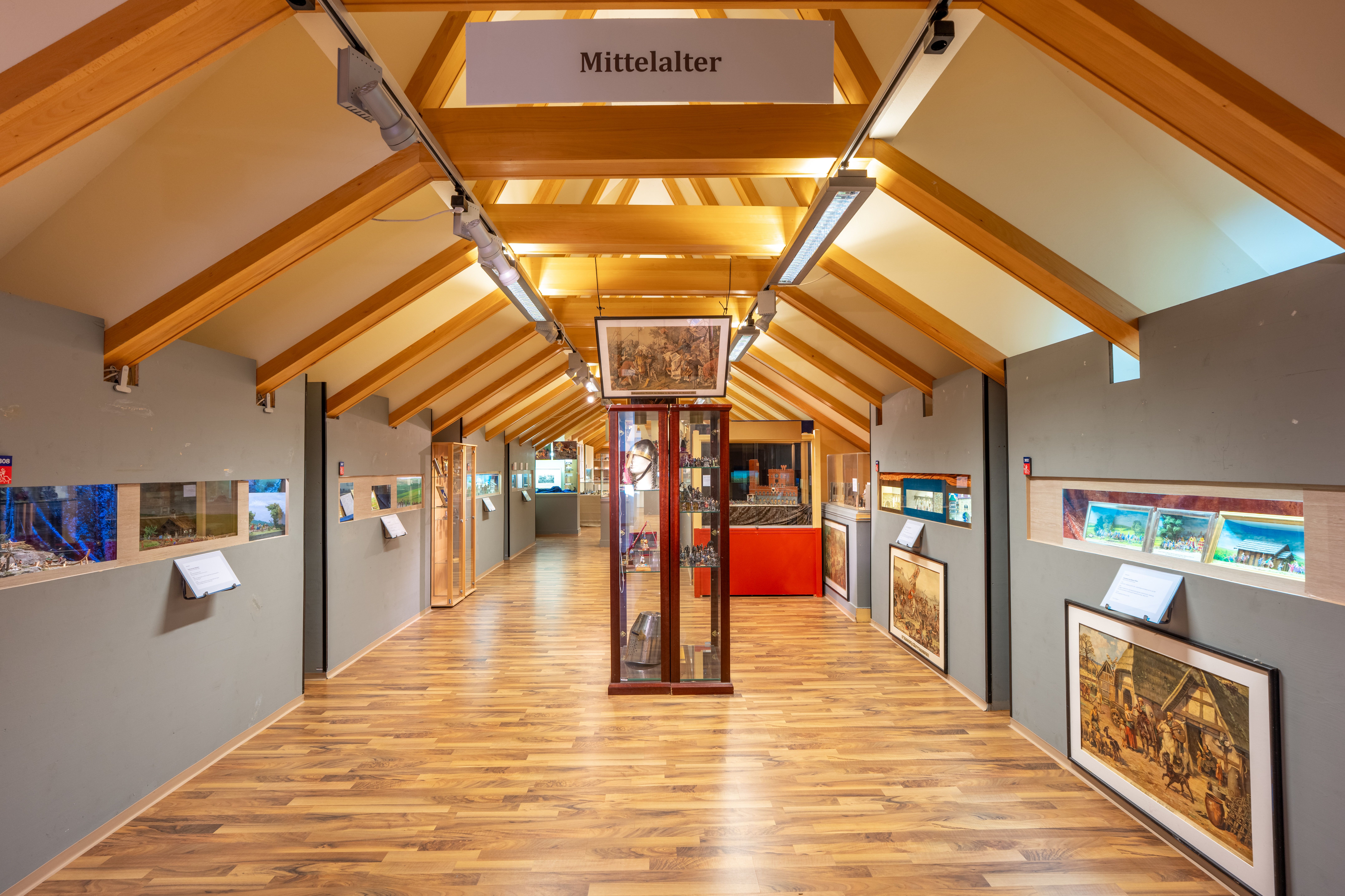 Ein Ausstellungsraum mit dem Thema Mittelalter, in dem Zinnfiguren und historische Darstellungen gezeigt werden.