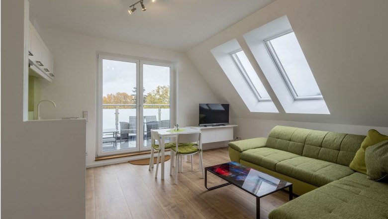 Modernes Wohnzimmer mit grüner Couch, Glastisch, TV und Balkonzugang.