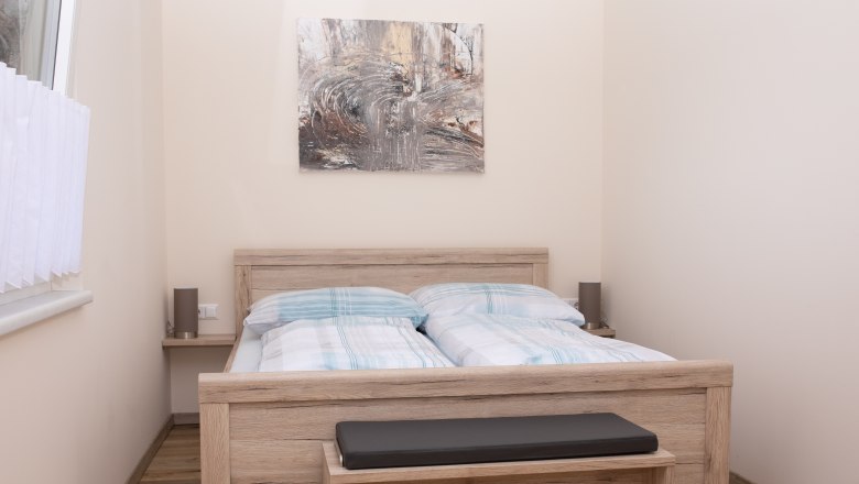 Schlafzimmer mit Doppelbett, Holzmöbeln und abstraktem Kunstwerk an der Wand.