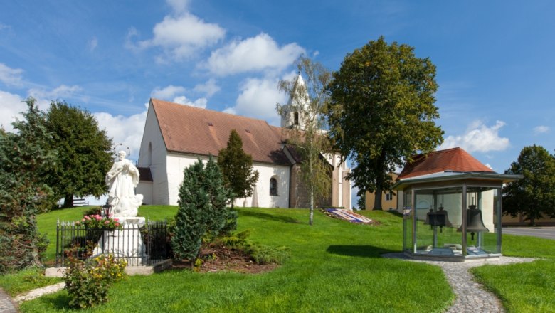 Wehrkirche St. Stephan mit Statue und Glockenhäuschen im Vordergrund.