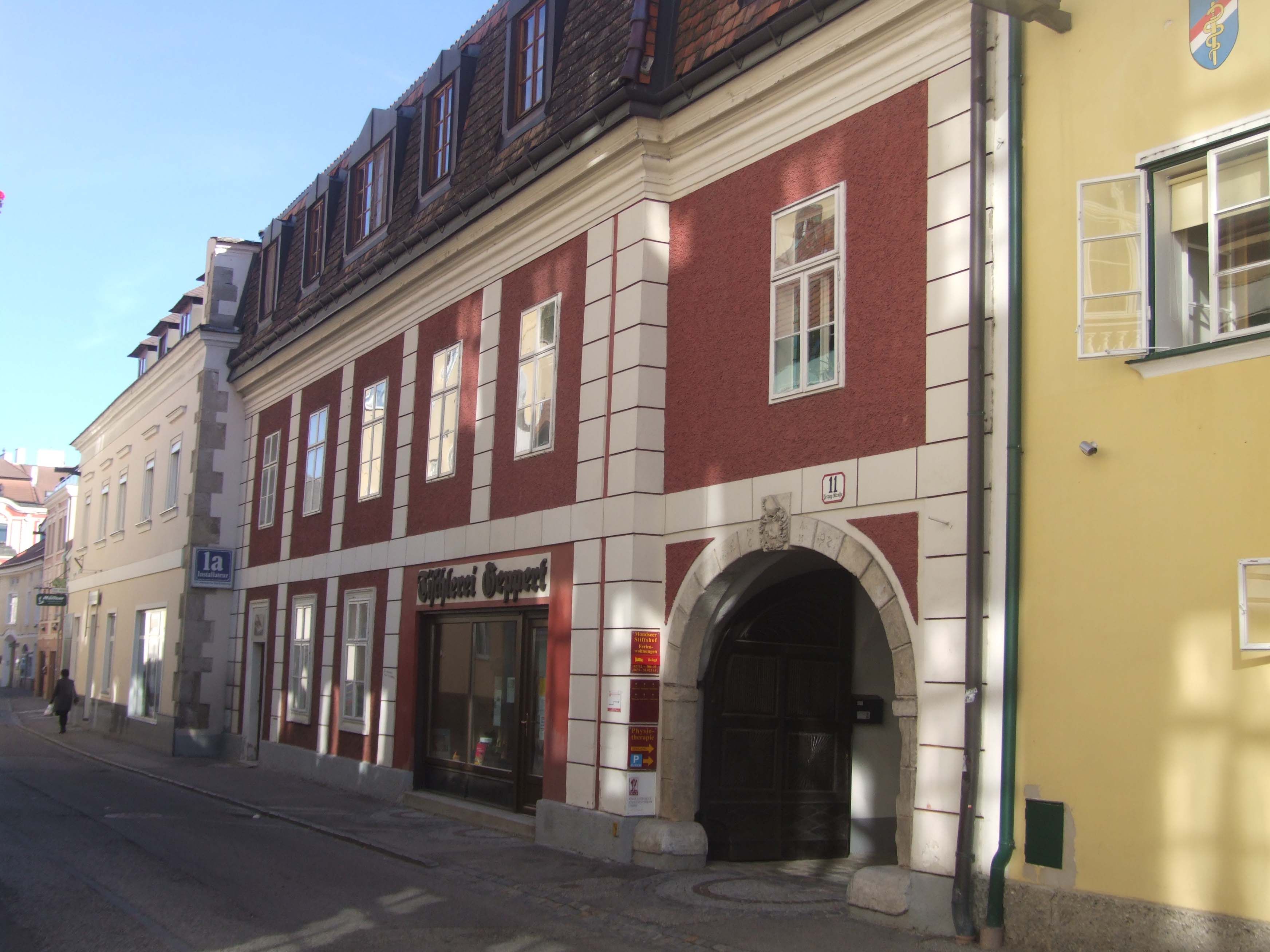 Historisches Gebäude mit roter Fassade und Torbogen in einer Straße.