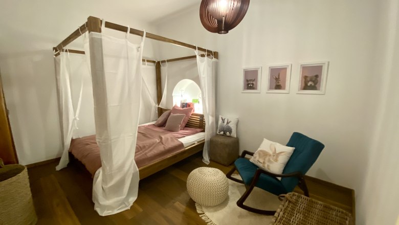 Gem&uuml;tliches Schlafzimmer mit Himmelbett, Schaukelstuhl und Tierbildern an der Wand.