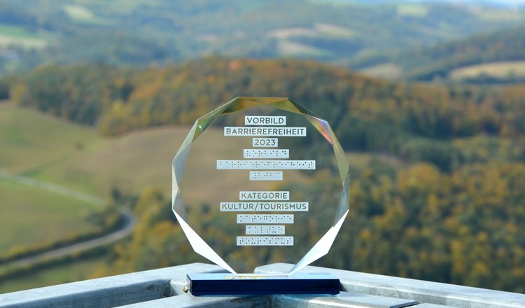 Eine Auszeichnung für Barrierefreiheit 2023 steht auf einem Geländer mit Landschaft im Hintergrund. Die Aussichtsplattform ist mit einem Aufzug erreichbar.