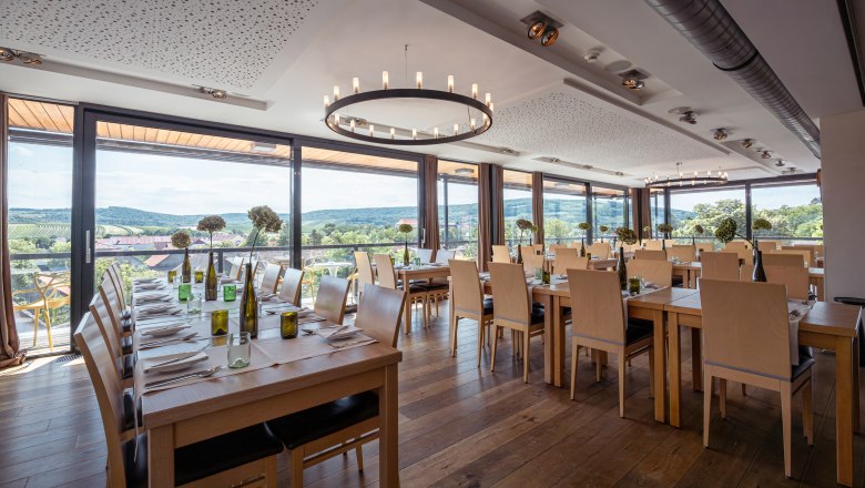 Innenansicht eines modernen Restaurants mit gro&szlig;en Fenstern und Blick auf Weinberge.