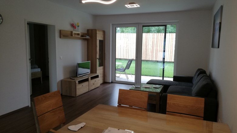 Modernes Wohnzimmer mit Holzm&ouml;beln, grauem Sofa und gro&szlig;em Fenster zum Garten.