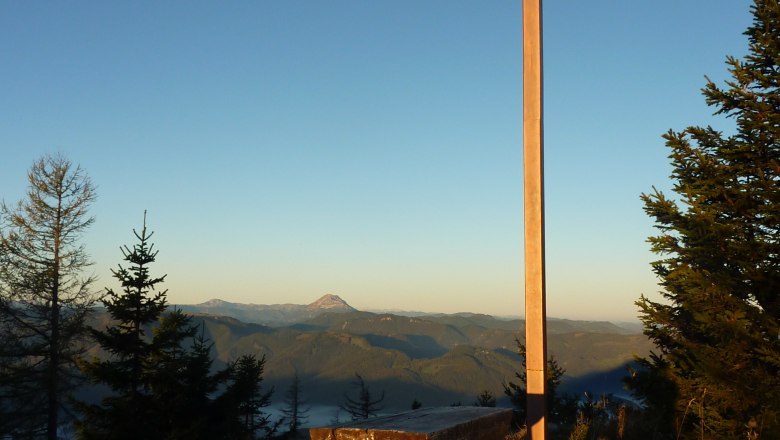 Gipfelkreuz am Türnitzer Höger mit Holzbänken und Bergpanorama im Hintergrund.