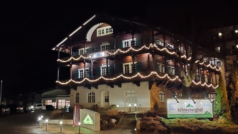 Ein beleuchtetes Geb&auml;ude namens Schneeberghof bei Nacht, dekoriert mit Lichterketten.