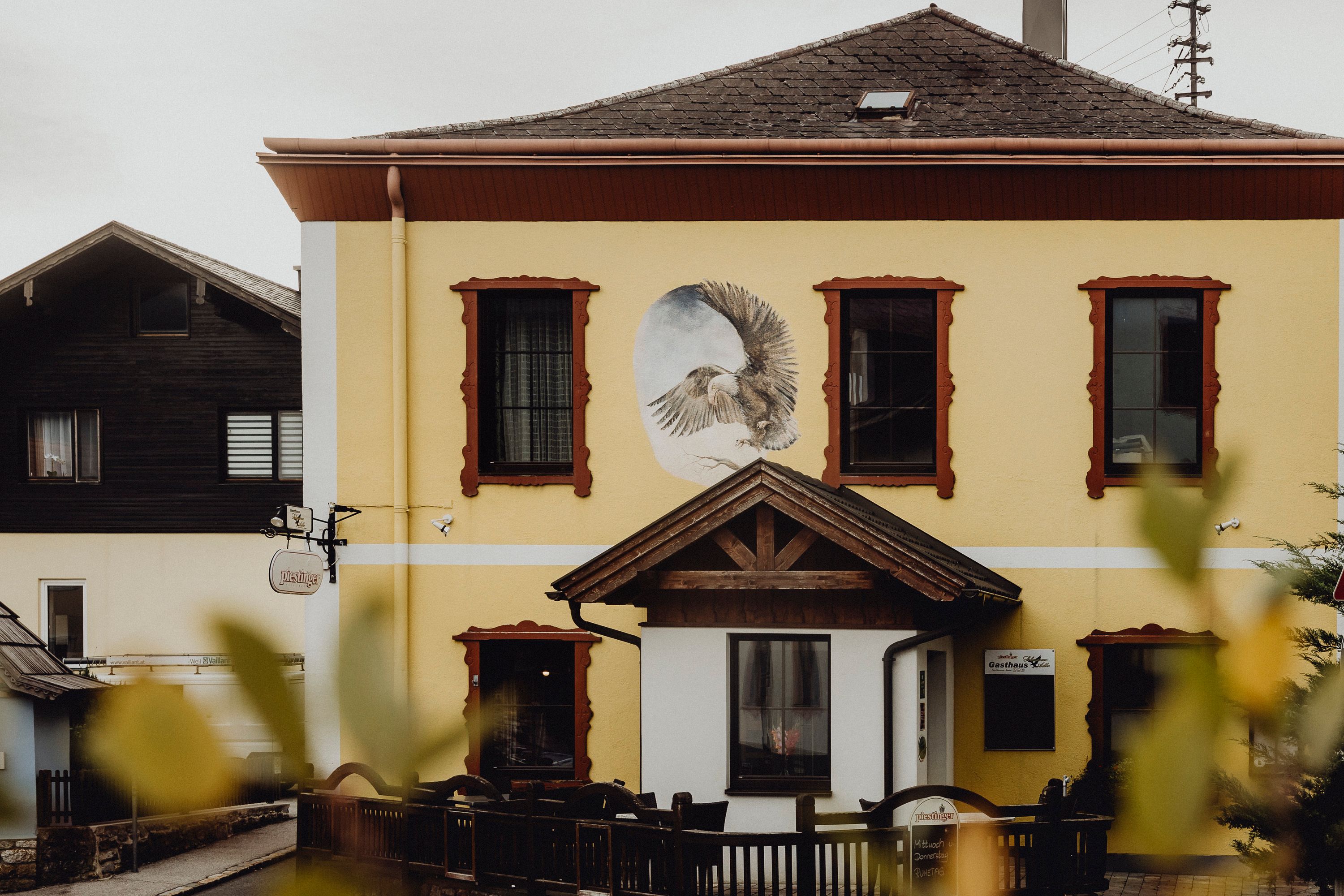 Gelbes Gebäude mit Wandgemälde eines Adlers und roten Fensterrahmen.