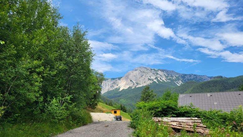 Zufahrt zu einem Tinyhouse in einer bergigen Landschaft mit blauem Himmel und Wolken.