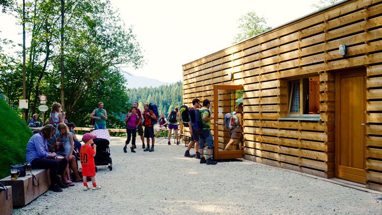Menschen vor einem modernen Holzgebäude in einer Waldumgebung.