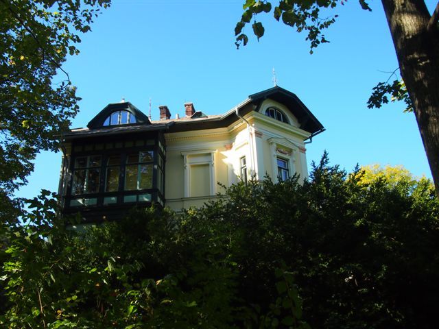 Historische Villa hinter Bäumen, blauer Himmel.
