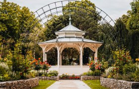 Weißer Pavillon hinter Rosenbogen