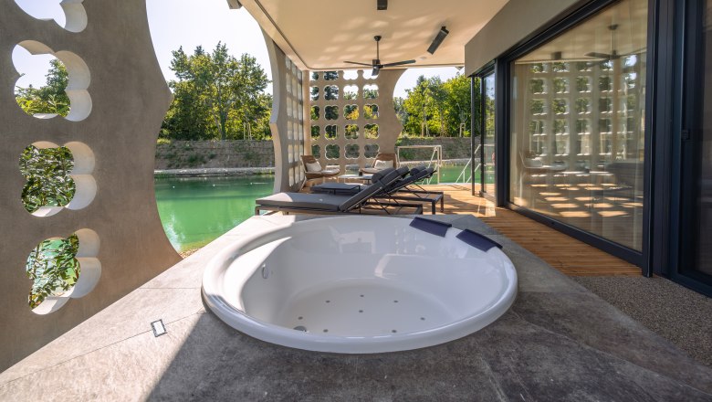 Terrasse mit Whirlpool und Liegest&uuml;hlen, Blick auf einen Teich.