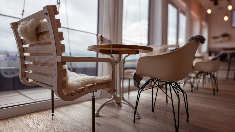 Innenansicht eines Caf&eacute;s mit modernen St&uuml;hlen und Holztisch, gro&szlig;e Fenster im Hintergrund.