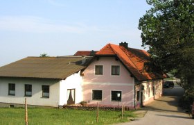 Ein traditionelles Gasthaus mit rosa und wei&szlig;en W&auml;nden und einem roten Ziegeldach, umgeben von gr&uuml;ner Landschaft.