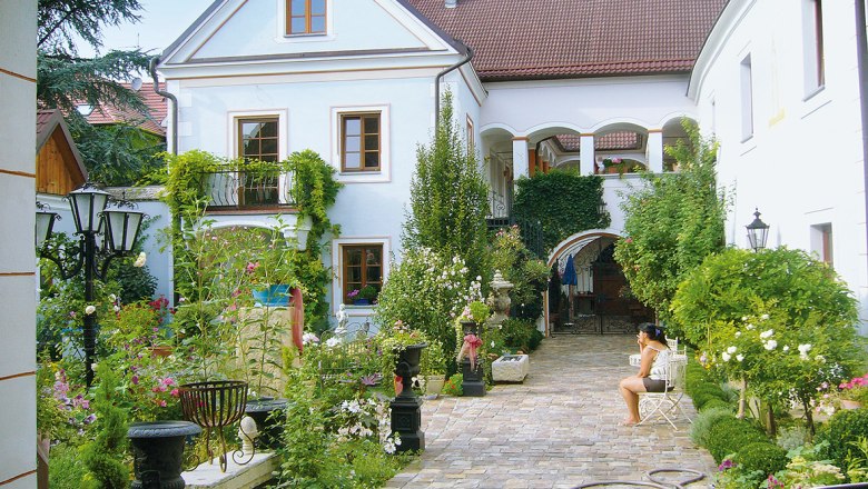 Ein idyllischer Innenhof mit Pflanzen und einer sitzenden Person.