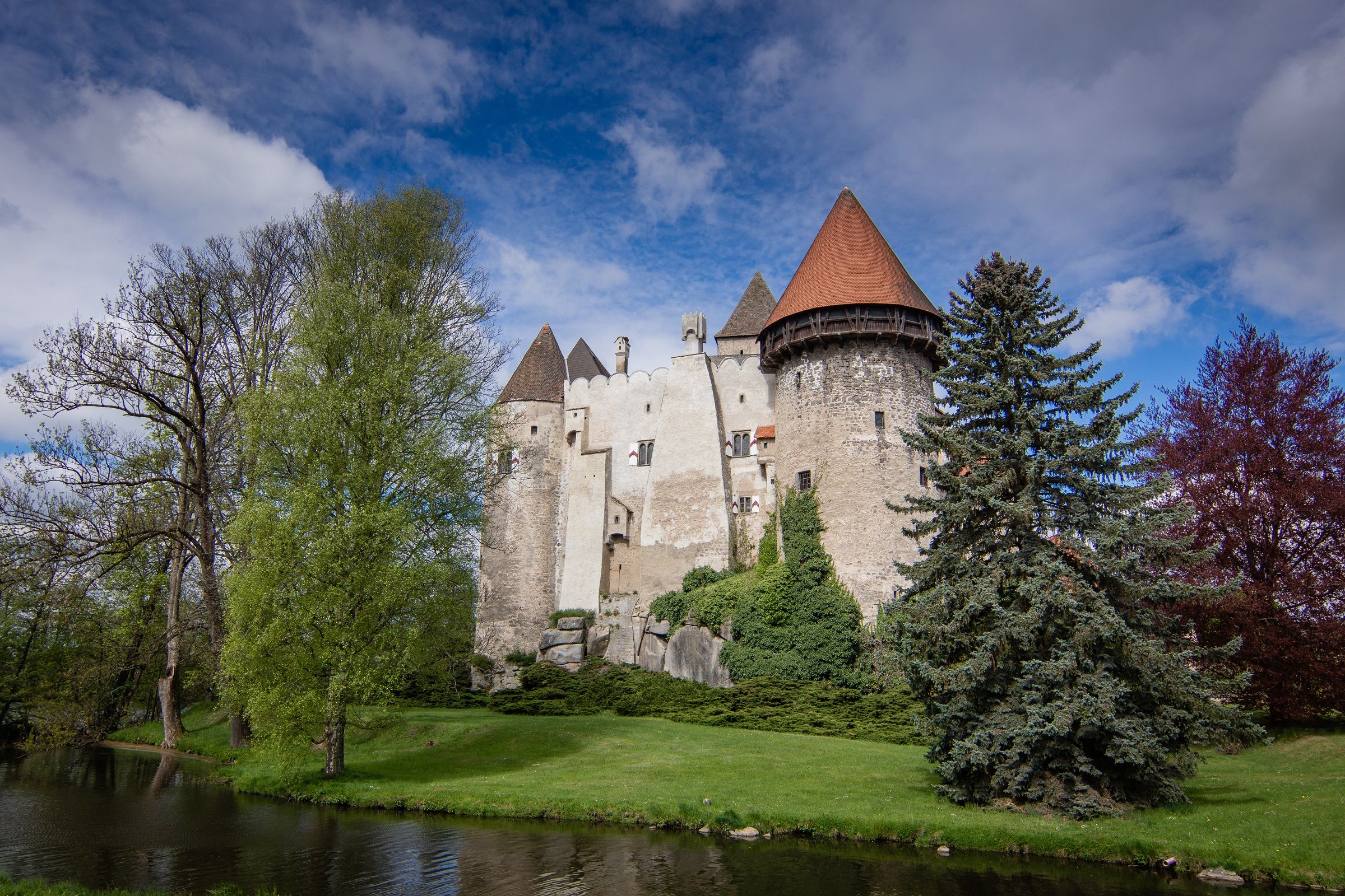 Burg Heidenreichstein mit Türmen und umgebenden Bäumen, vor blauem Himmel.