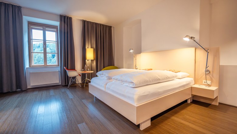 Modernes Schlafzimmer mit Doppelbett, Holzfu&szlig;boden und Fenster mit Vorh&auml;ngen.