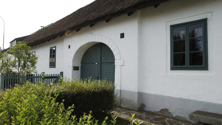 Das Geburtshaus von Joseph Haydn in Rohrau, ein wei&szlig;es Geb&auml;ude mit Strohdach und gr&uuml;ner T&uuml;r.