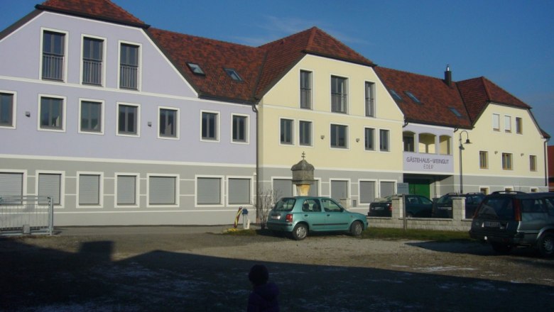 Ein modernes G&auml;stehaus mit roten D&auml;chern und pastellfarbenen Fassaden, Autos im Vordergrund.