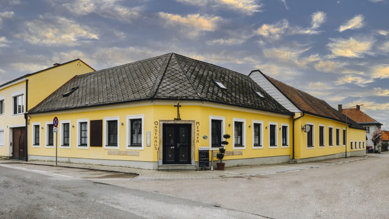 Gelbes Gasthaus an Straßenecke mit bewölktem Himmel im Hintergrund.