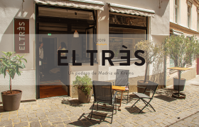 Außenansicht eines Cafés mit dem Namen EL TRÈS, Sitzgelegenheiten und Pflanzen vor dem Eingang.