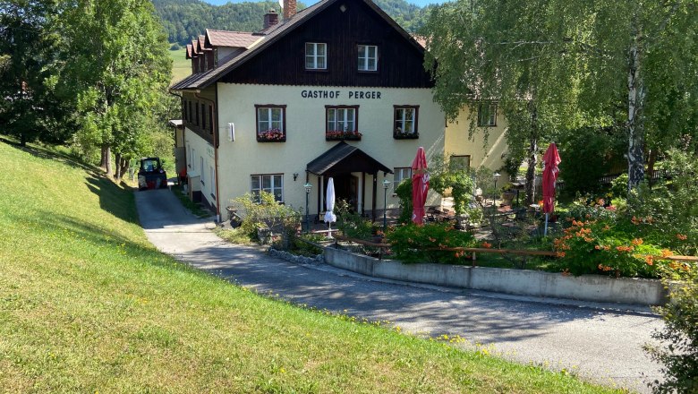 Ein traditionelles Gasthaus mit Terrasse und Sonnenschirmen, umgeben von gr&uuml;ner Landschaft.