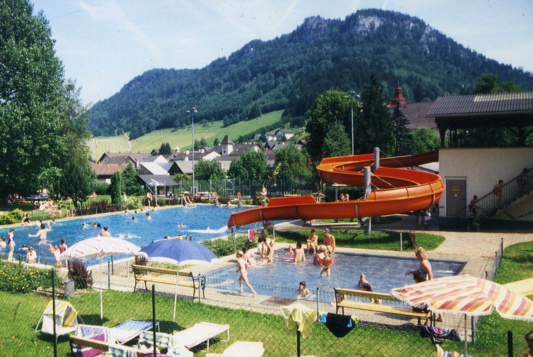Freibad mit Rutsche und Berglandschaft im Hintergrund.