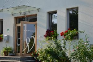 Eingang eines Gebäudes mit der Aufschrift 'wein + bett', umgeben von Blumen.