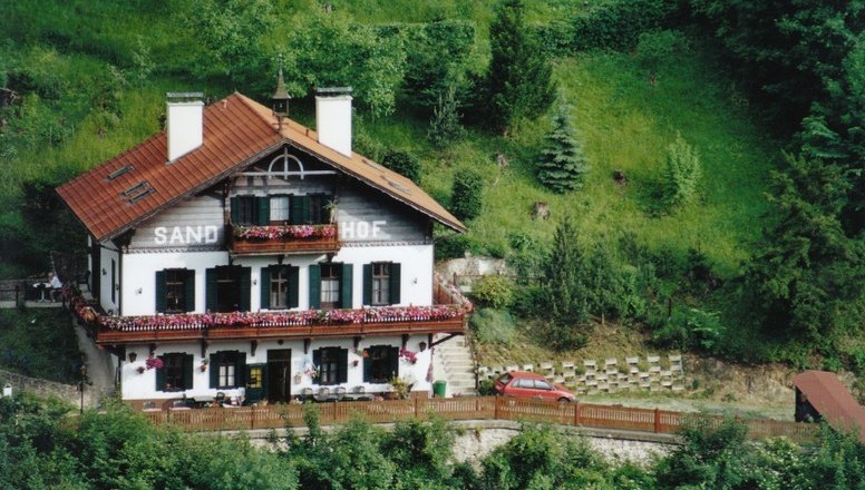Traditionelles Haus namens Sand-Hof in grüner Landschaft.
