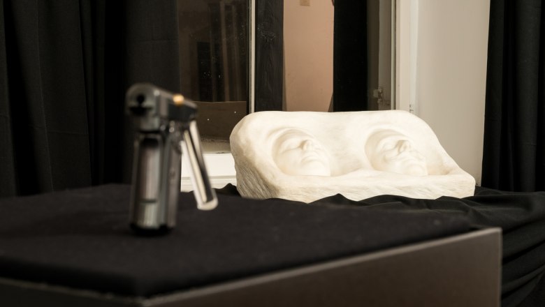 Skulptur mit zwei Gesichtern und unscharfem Objekt im Vordergrund.