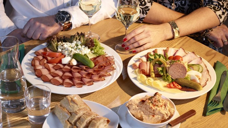 Zwei Personen sitzen an einem Tisch mit Wurst- und K&auml;seplatten, Brot und Wein.