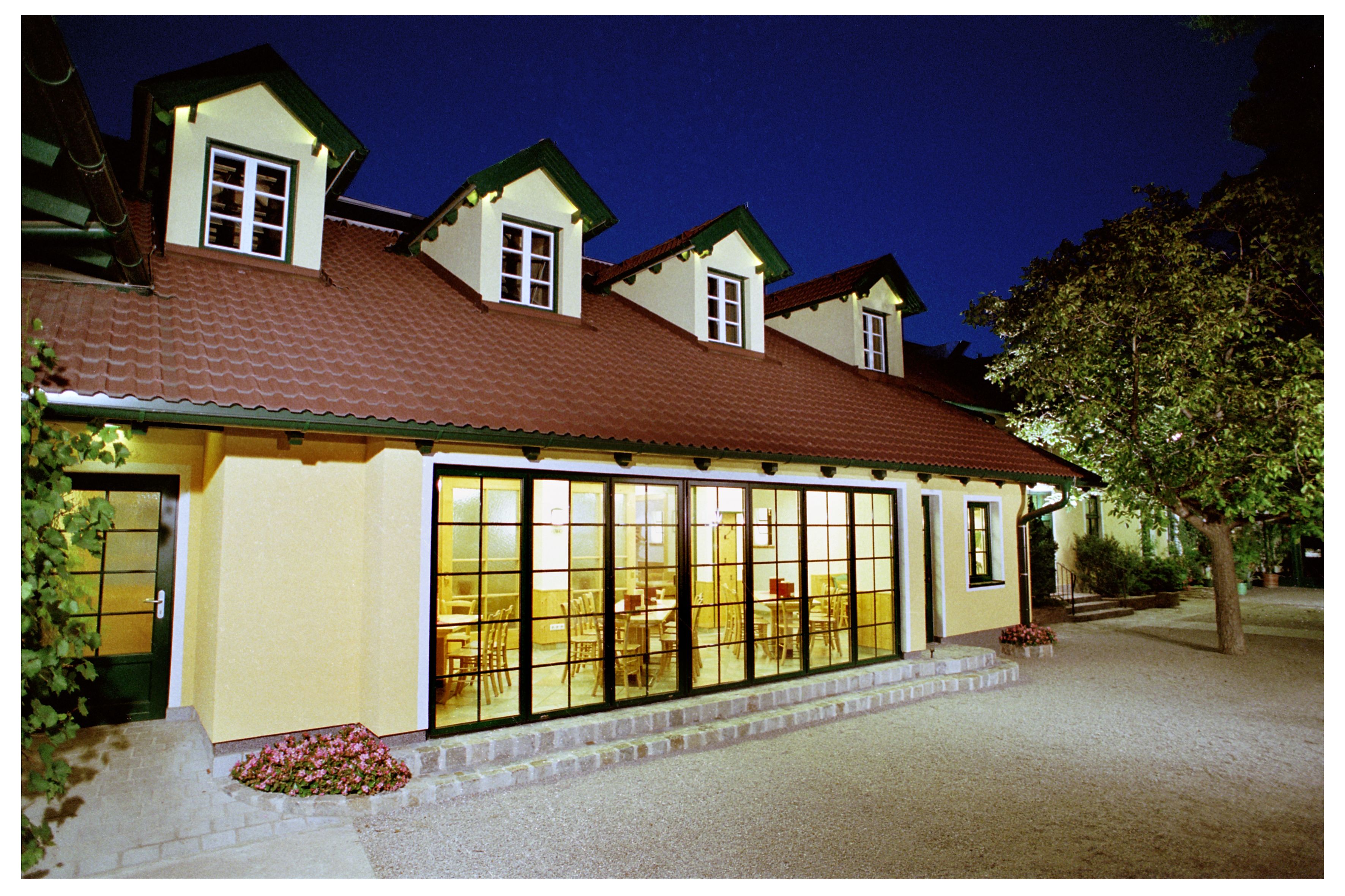 Ein Gebäude mit gelber Fassade und roten Dachziegeln bei Nacht, beleuchtet von innen.