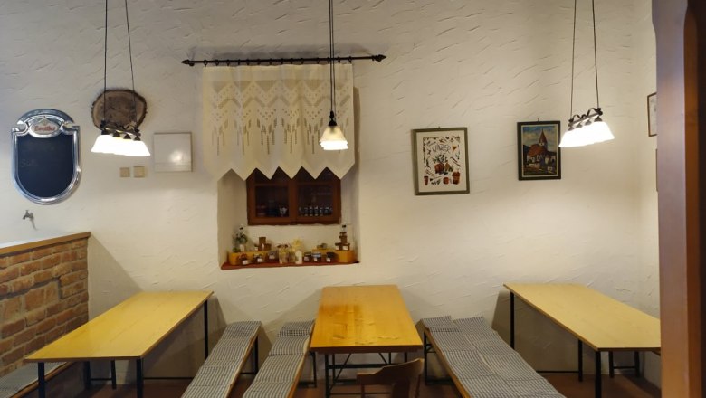 Gem&uuml;tliche Stube mit Holztischen und B&auml;nken, dekoriert mit Bildern und Lampen.