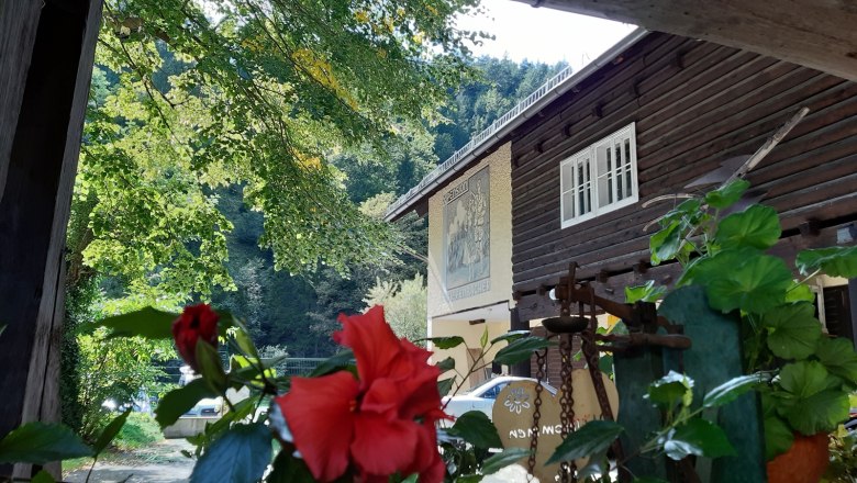 Idyllischer Hof, © Familie Kellner Ein traditionelles Holzhaus mit roten Blumen im Vordergrund und grünen Bäumen im Hintergrund.