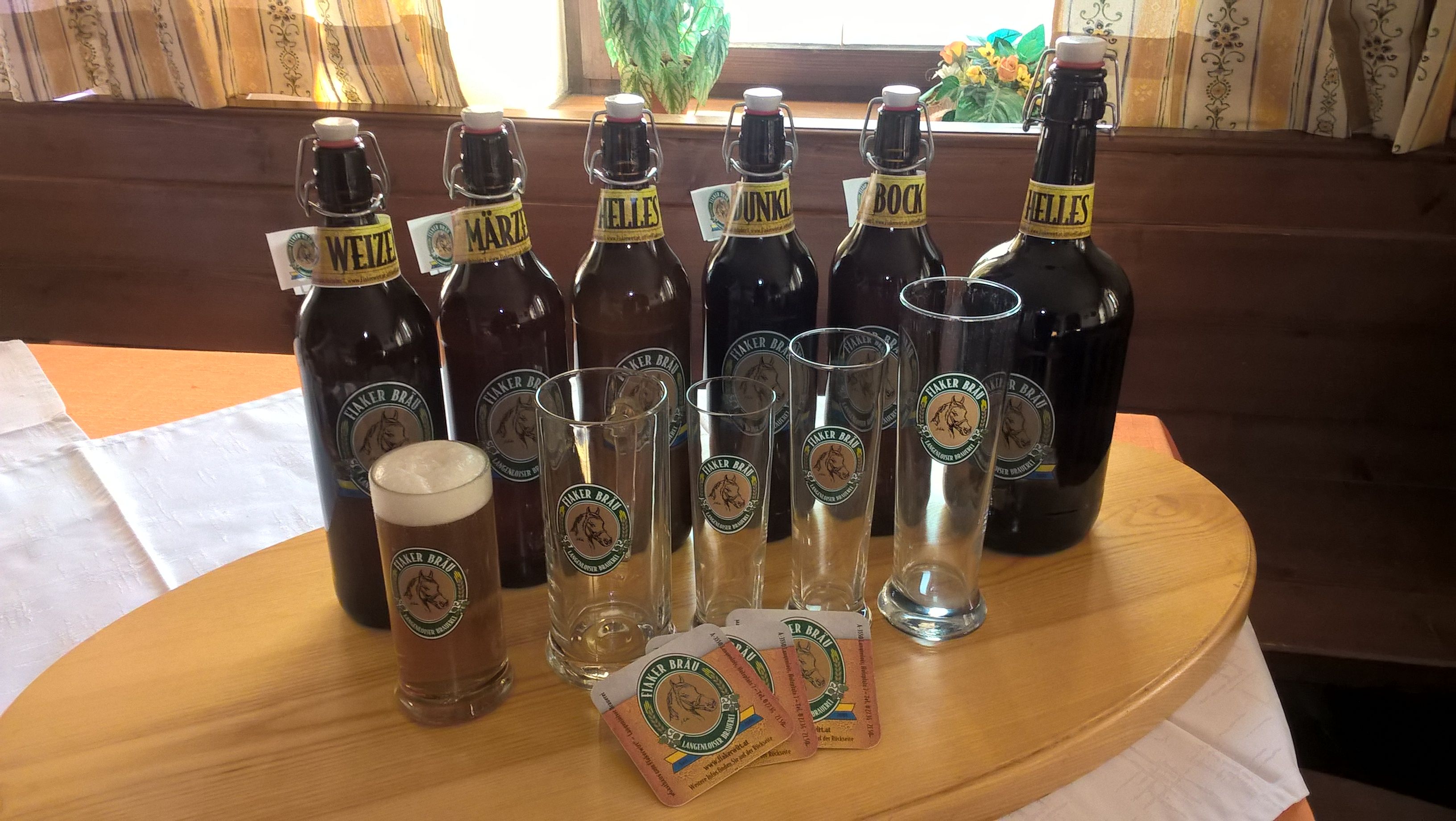 Verschiedene Bierflaschen und Gläser der Marke Fiaker Bräu auf einem Tisch.