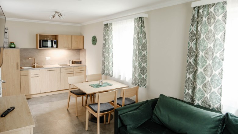 Moderne K&uuml;che mit Holzm&ouml;beln, Esstisch, gr&uuml;nen Vorh&auml;ngen und Sofa.