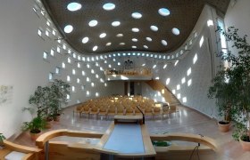 Moderner Kircheninnenraum mit runden Fenstern und Holzm&ouml;beln.