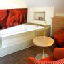 Gem&uuml;tliches Zimmer mit Badewanne, roten Sesseln und Rosenbild an der Wand.