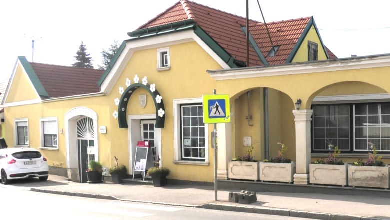 Au&szlig;enansicht eines gelben Geb&auml;udes mit Arkaden und rotem Dach.