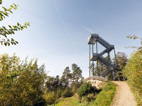 Die Aussichtswarte erhebt sich majest&auml;tisch &uuml;ber die umliegenden W&auml;lder und bietet einen atemberaubenden Blick auf die sanften H&uuml;gel der Region. Umgeben von &uuml;ppigem Gr&uuml;n und dem Gesang der V&ouml;gel, l&auml;dt dieser Ort zum Verweilen und Entspannen ein. Hier wird der Sommer in den Bergen zum unvergesslichen Erlebnis.