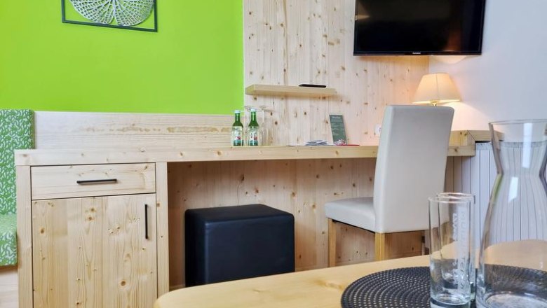 Ein Hotelzimmer mit Holzmöbeln, einem Schreibtisch, einem Fernseher an der Wand und einer grünen Wanddekoration.