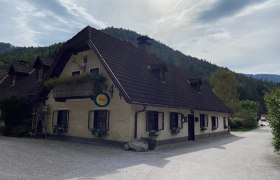 Traditionelles Gasthaus mit Blumenbalkon vor bewaldeten Hügeln.