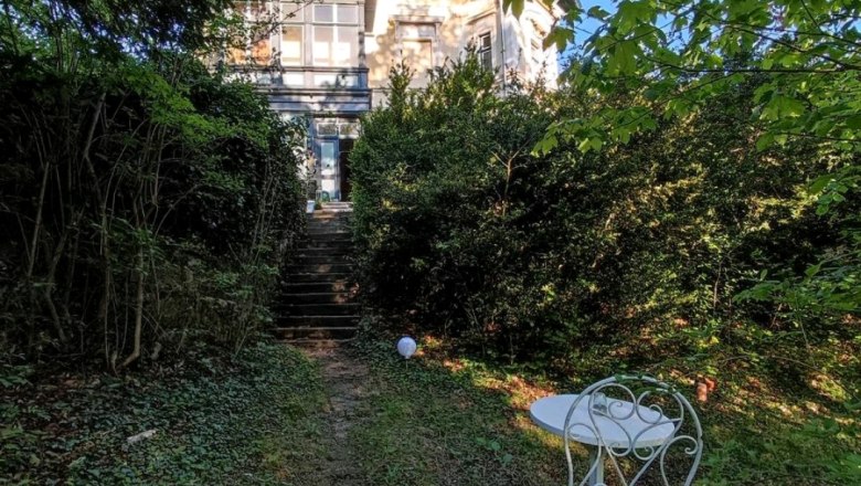 Ein altes Herrenhaus mit Garten und Gartenmöbeln im Vordergrund.