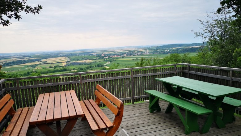Aussichtsplattform mit Holzb&auml;nken und Tischen, Blick auf weite Landschaft und Felder.