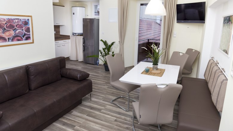 Moderne K&uuml;che mit braunem Sofa, Esstisch und St&uuml;hlen, K&uuml;hlschrank und Pflanzen.