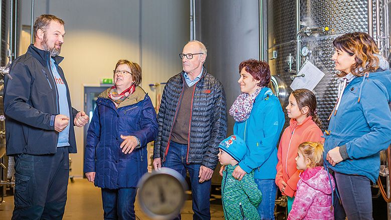 Gruppe von Menschen in einer Fabrikhalle mit großen Metalltanks.