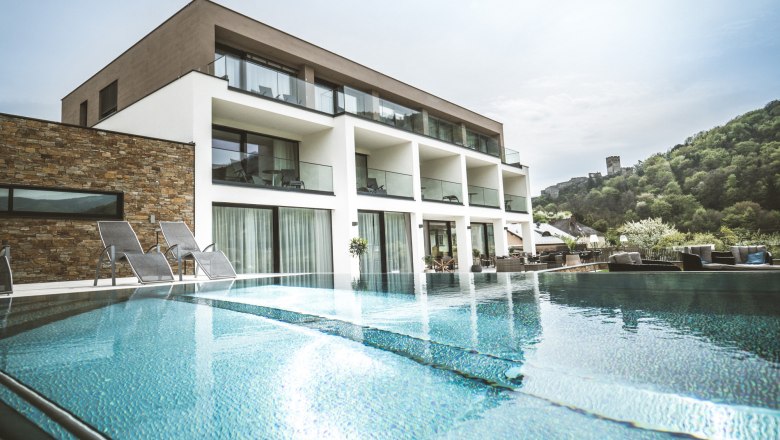 Modernes Boutiquehotel mit Pool und Liegest&uuml;hlen, umgeben von gr&uuml;ner Landschaft.