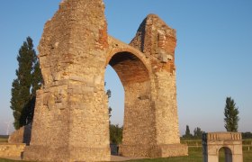 Heidentor in Petronell-Carnuntum, ein antikes römisches Monument aus Stein mit einem Bogen, umgeben von grüner Landschaft.