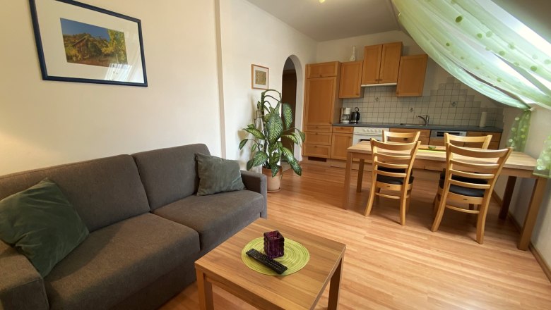 Wohnzimmer mit grauem Sofa, Holztisch, Esstisch und K&uuml;che im Hintergrund.